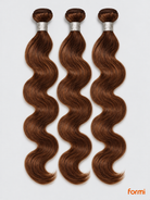 Three #30 auburn body wave human hair bundles with silver wraps on a pale gray background.