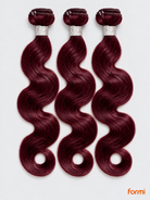 Three 99J burgundy body wave human hair bundles with silver wraps on a pale gray background.