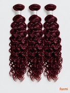 Three 99J burgundy water wave human hair bundles with silver wraps on a pale gray background.