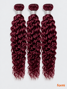 Three 99J burgundy water wave human hair bundles with silver wraps on a pale gray background.